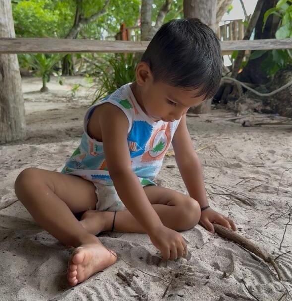 Child drawing lines in wet sand with a small stick